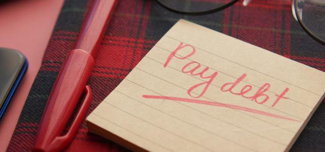 a note that says pay debt next to a pen and glasses by Towfiqu barbhuiya courtesy of Unsplash.